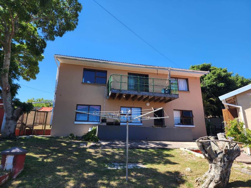 Rear view of a two-story house featuring a balcony with metal railings, a concrete patio area, and established garden surroundings.
