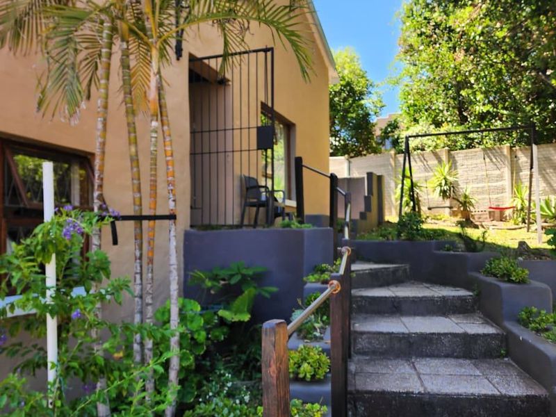 Rear exterior view featuring stone steps with metal handrails, landscaped retaining walls, and a secure gated entrance to the property.