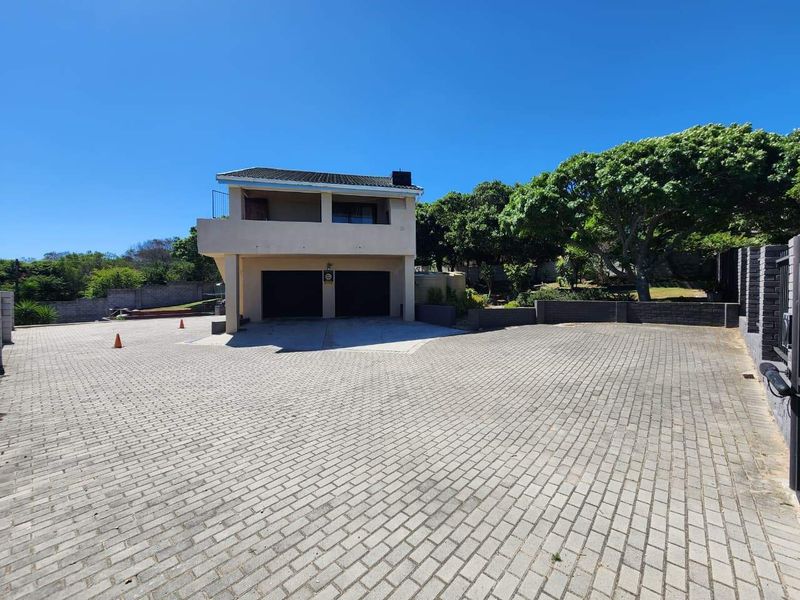Front view of a two-story house featuring a double garage, a spacious paved driveway, and an upper-level balcony.