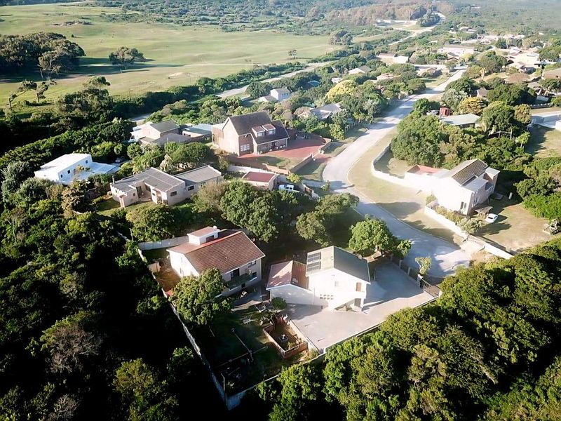 An aerial view of a residential neighborhood featuring multiple houses with tiled roofs, paved driveways, and surrounding greenery.