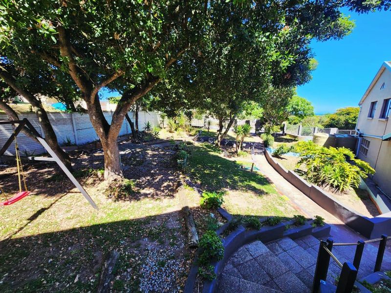 A spacious backyard garden featuring mature trees, tiered retaining walls, paved stairs, and a concrete boundary wall.