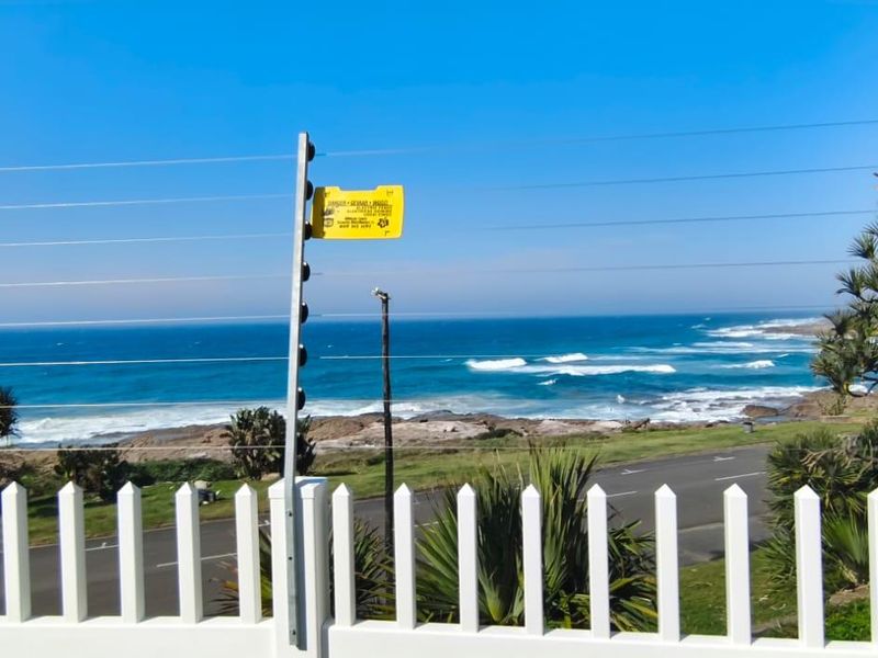 A scenic coastal view overlooking the ocean and shoreline, framed by a white picket fence and security electric fencing.