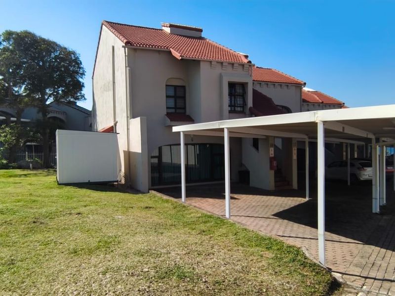 Exterior view of the apartment building featuring a covered carport, paved driveway, and surrounding lawn area with coastal views.