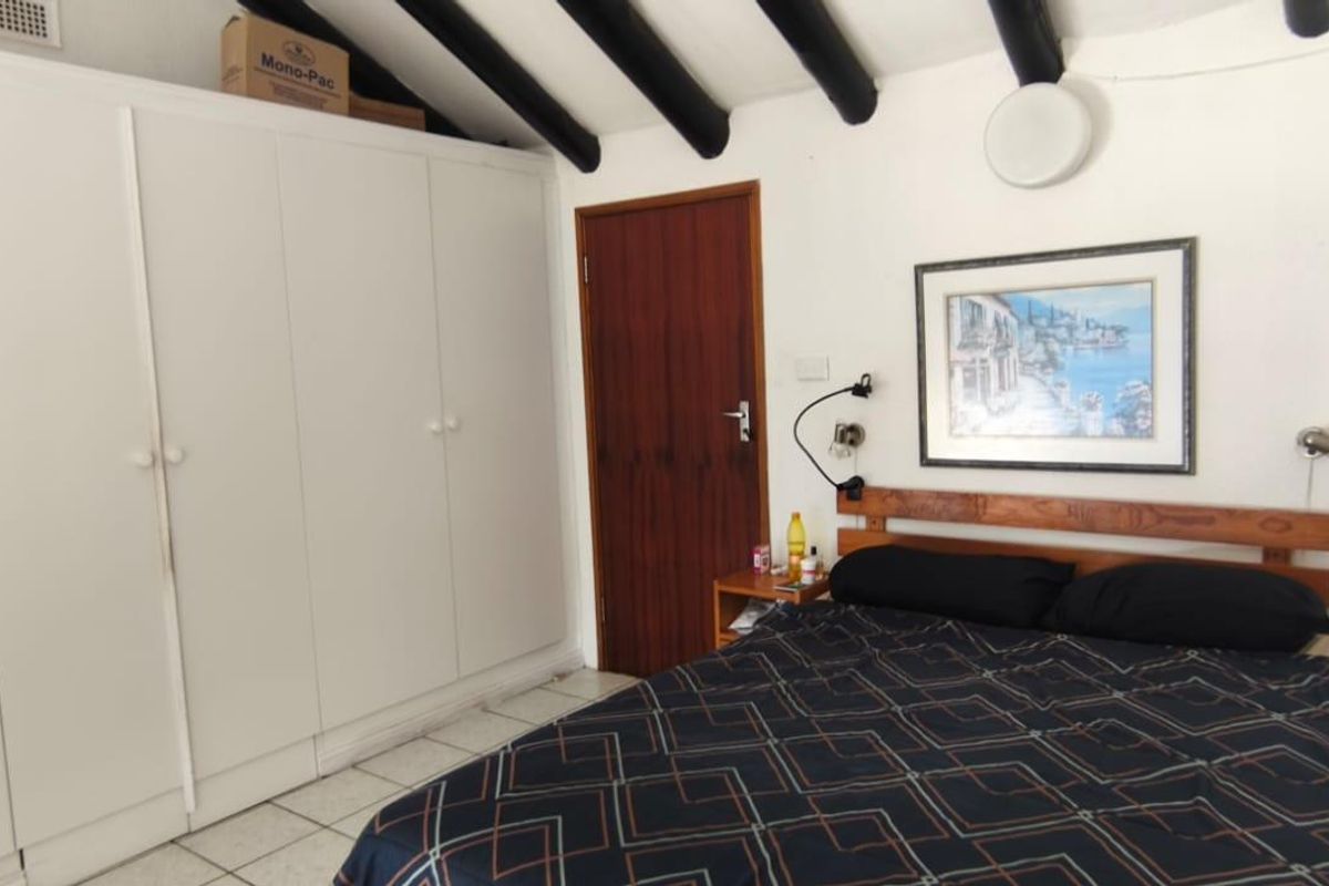 A bedroom featuring built-in cupboards, exposed ceiling beams, and tiled flooring, offering a functional space with potential for modern updates.