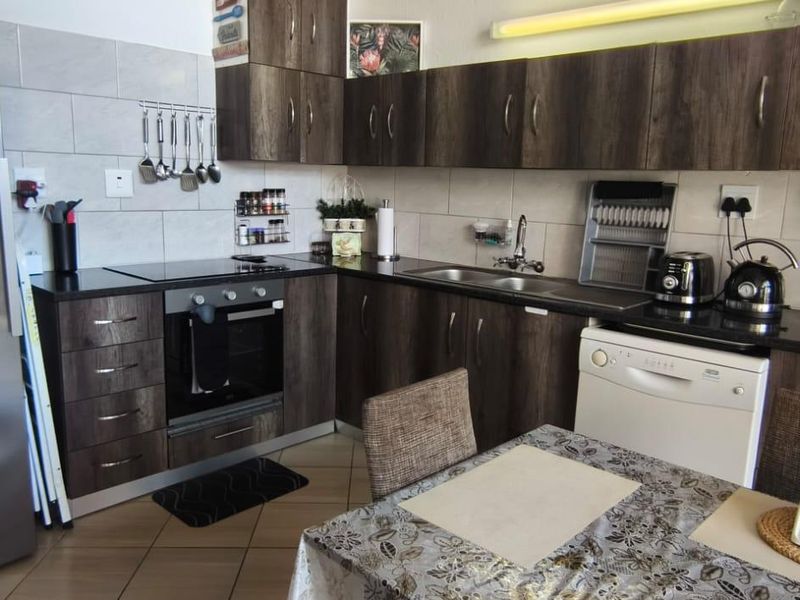 A functional kitchen featuring dark wood-finish cabinetry, laminate countertops, a built-in oven with electric hob, and tiled backsplash.