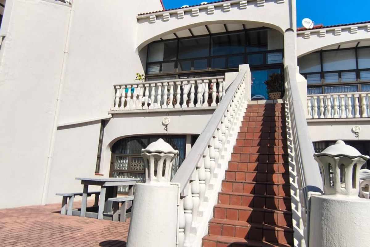 Rear exterior view of the apartment complex featuring a paved patio area, a central staircase with balustrades, and upper-level balcony access.