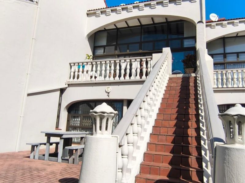 Rear exterior view of the apartment complex featuring a paved patio area, a central staircase with balustrades, and upper-level balcony access.