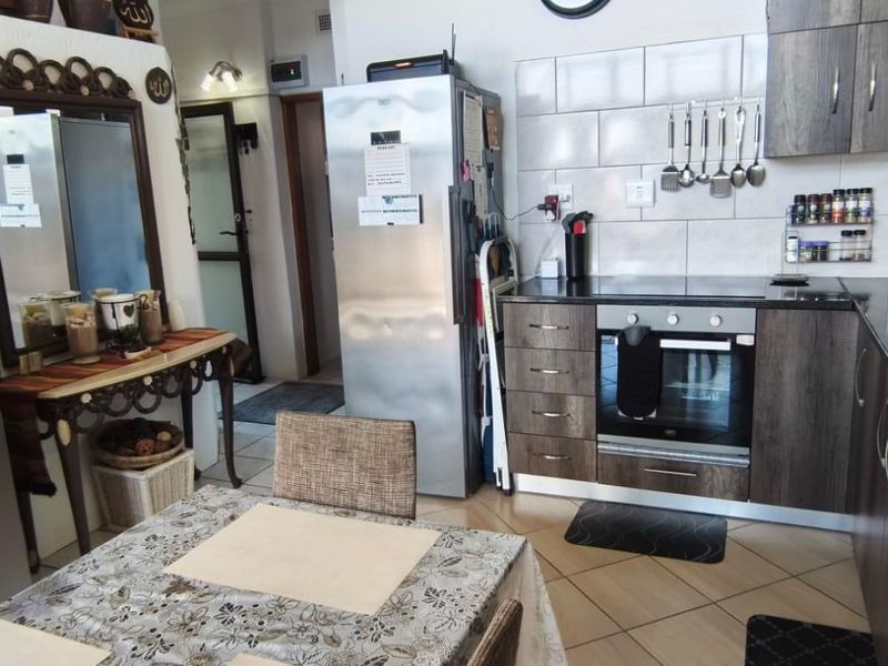 A functional kitchen featuring dark wood-finish cabinetry, a built-in oven and hob, tiled backsplash, and a double basin sink with tiled flooring.
