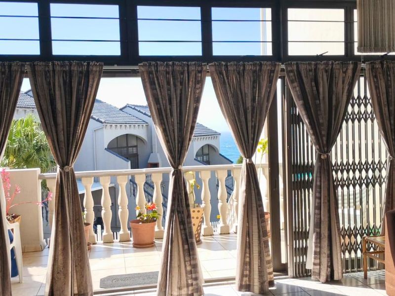 A balcony area featuring tiled flooring, a balustrade, and sliding glass doors with security gates, offering an outdoor space with coastal views.