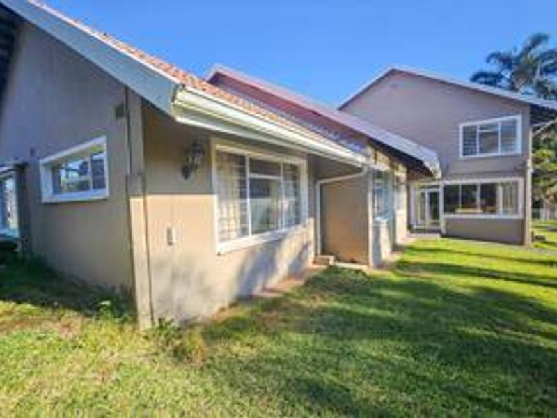 Rear view of the property featuring a tiled roof, aluminium window frames with security bars, and a surrounding lawn area.