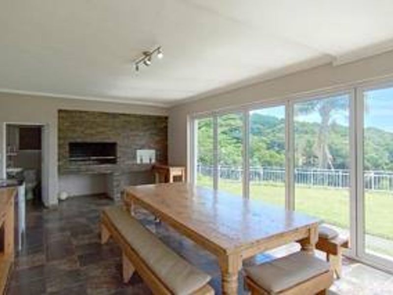 Open-plan entertainment area featuring a built-in braai with stone cladding, tiled floors, and large sliding doors opening to a scenic garden view.