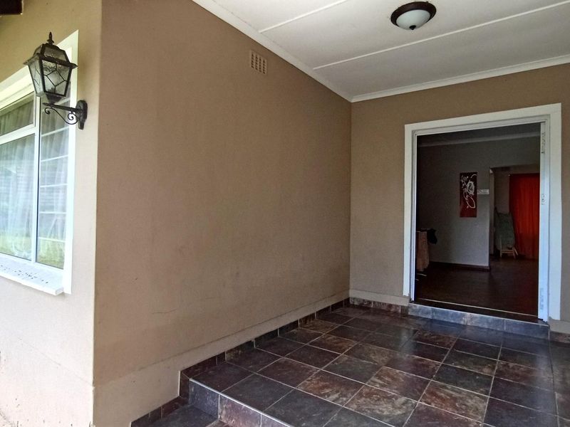 A covered patio area featuring tiled flooring, a wall-mounted light fixture, and access to the interior of the home.