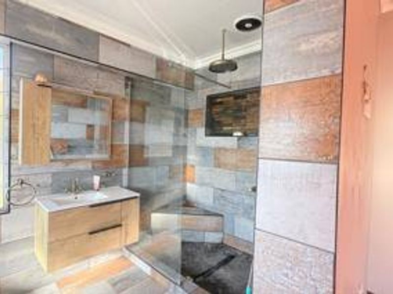 Modern bathroom featuring a floating vanity, large walk-in shower with a rain shower head, and contemporary multi-toned wall tiling.