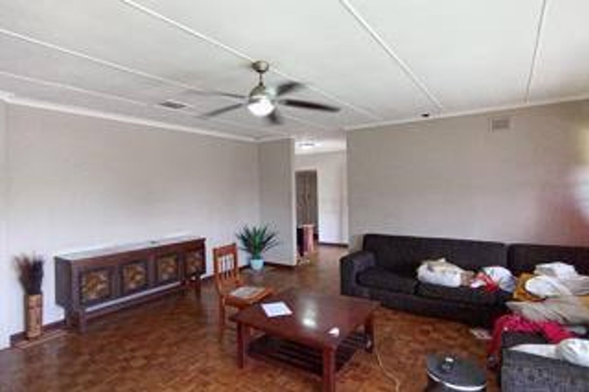 A spacious living room featuring classic parquet flooring, a central ceiling fan, and neutral wall finishes, offering a versatile layout for comfortable family living.