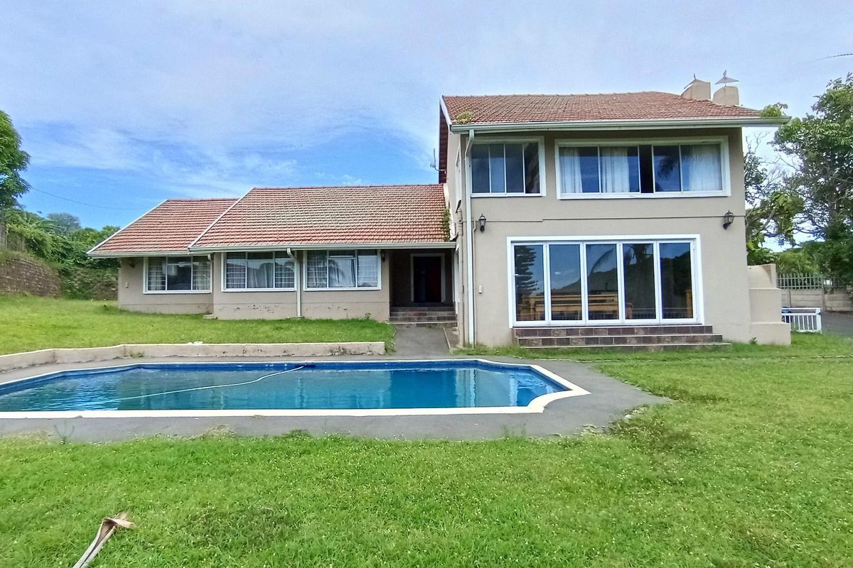 Rear view of a two-story house featuring a swimming pool, concrete patio area, and a large lawn set against a tiled roof facade.