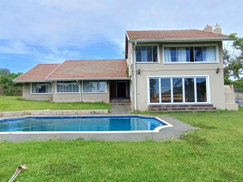 Rear view of a two-story house featuring a swimming pool, concrete patio area, and a large lawn set against a tiled roof facade.
