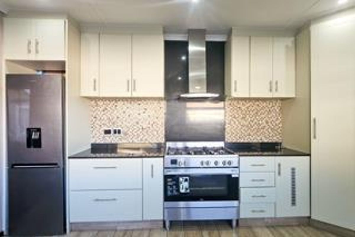 Modern kitchen featuring white cabinetry, stone countertops, a tiled backsplash, and a stainless steel gas stove with an integrated extractor fan.