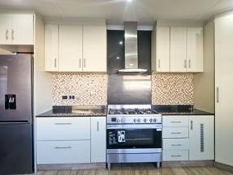 Modern kitchen featuring white cabinetry, stone countertops, a tiled backsplash, and a stainless steel gas stove with an integrated extractor fan.