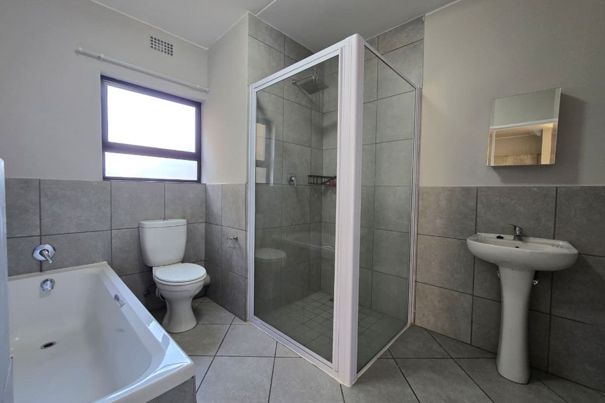 A clean, functional bathroom featuring a separate shower enclosure, bathtub, pedestal basin, and toilet with neutral grey wall and floor tiling.