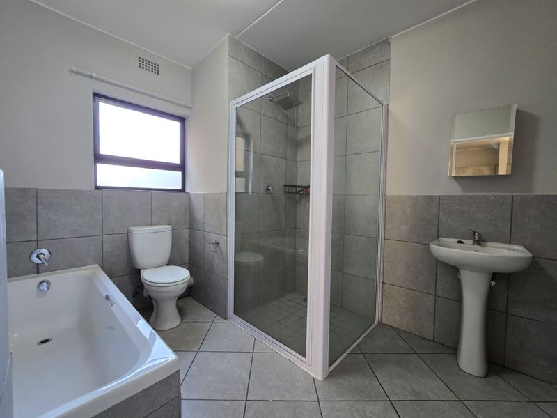 A clean, functional bathroom featuring a separate shower enclosure, bathtub, pedestal basin, and toilet with neutral grey wall and floor tiling.