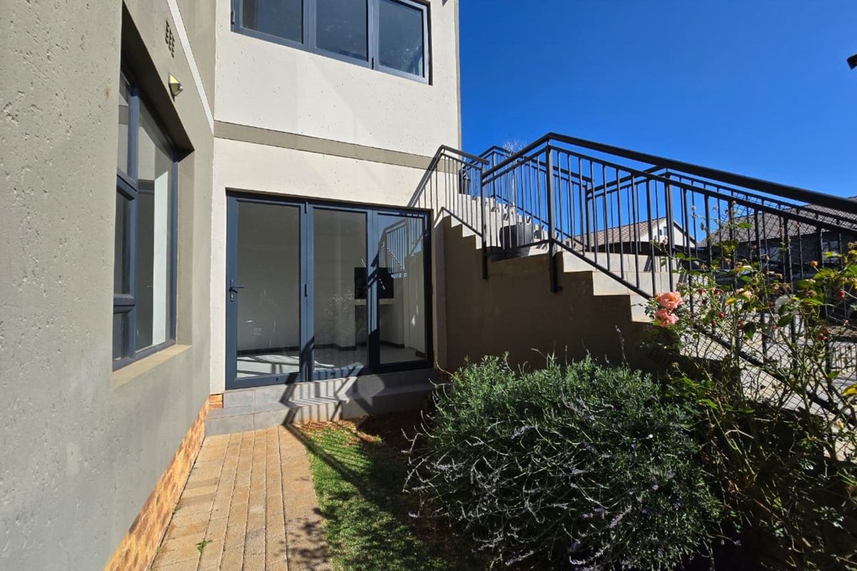 Rear exterior view of the townhouse featuring a paved walkway, external staircase with metal railing, and modern aluminium framed glass doors.
