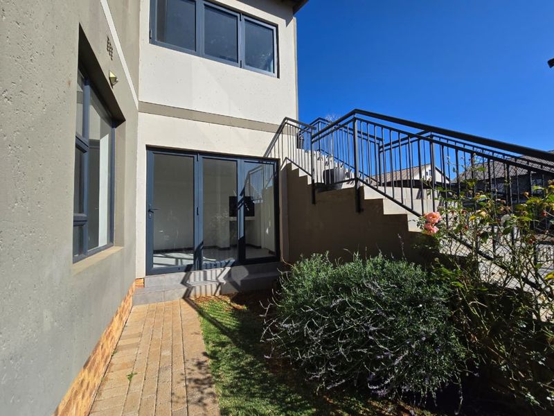 Rear exterior view of the townhouse featuring a paved walkway, external staircase with metal railing, and modern aluminium framed glass doors.