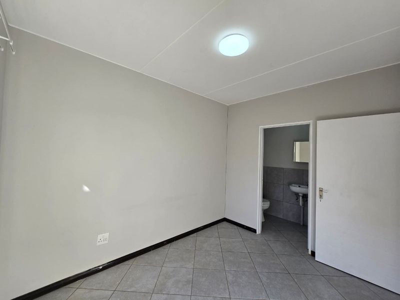 An empty bedroom featuring neutral wall paint, tiled flooring, and an adjoining en-suite bathroom.