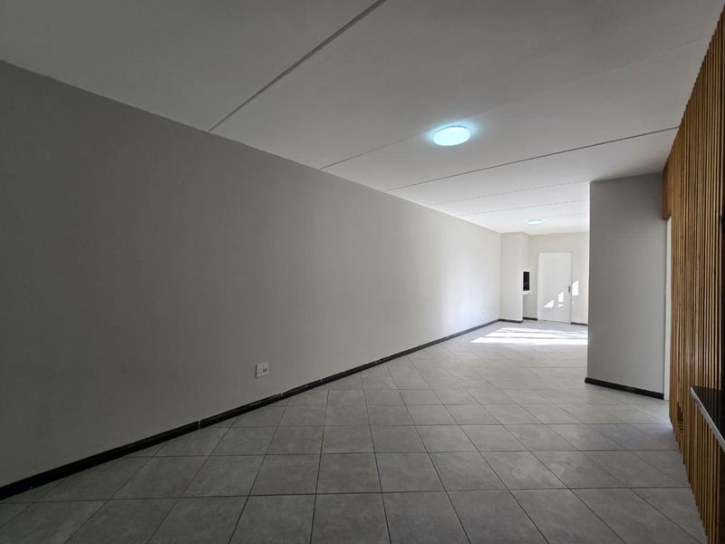 A spacious, empty open-plan living area featuring neutral tiled flooring, clean walls, and recessed ceiling lighting, offering a versatile blank canvas for interior design.
