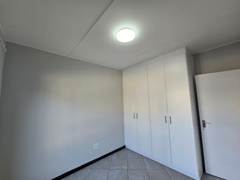 A clean, empty bedroom featuring neutral grey walls, tiled flooring, and white built-in cupboards providing ample storage space.