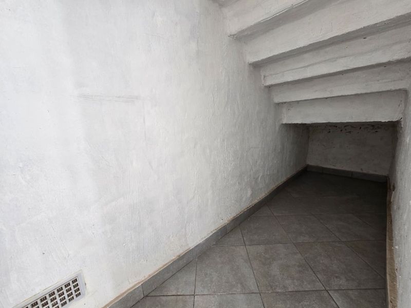 A small, empty utility storage space located under a staircase, featuring tiled flooring and a ventilation grille.