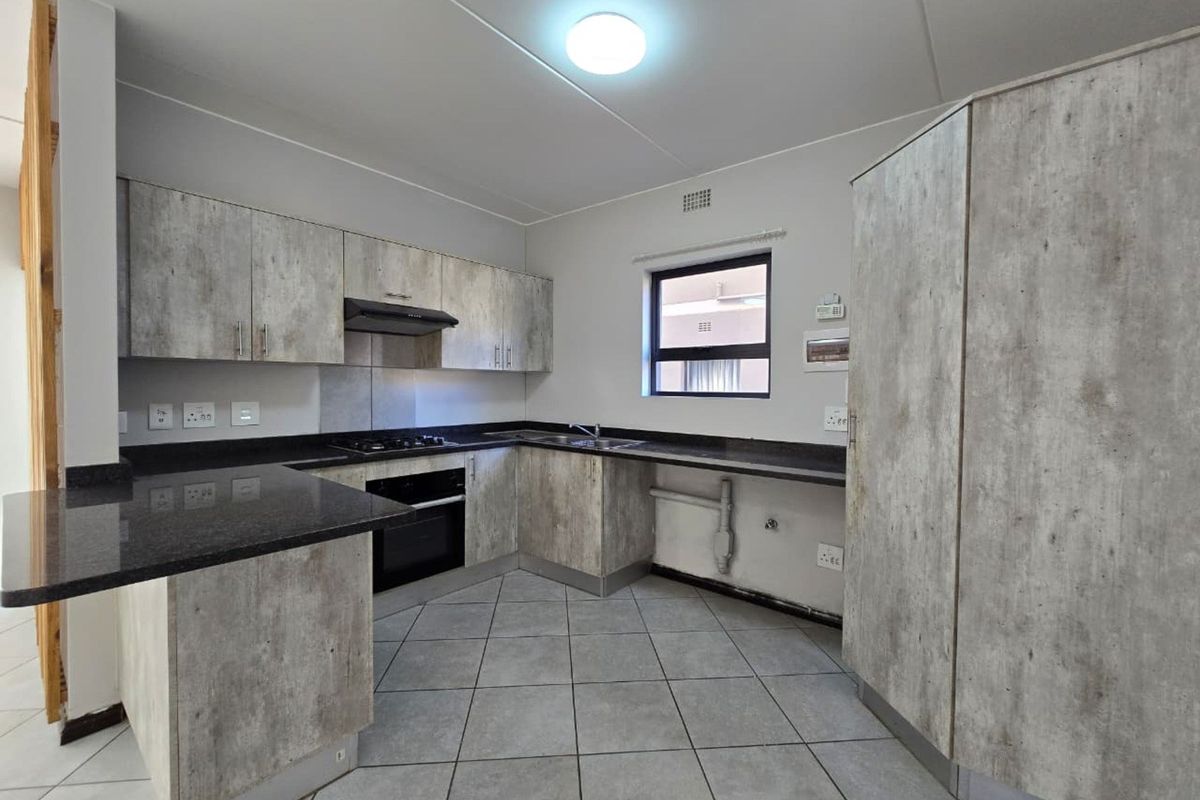 A functional kitchen featuring modern wood-look cabinetry, granite countertops, built-in oven, gas hob, and tiled flooring, offering a clean and practical workspace.