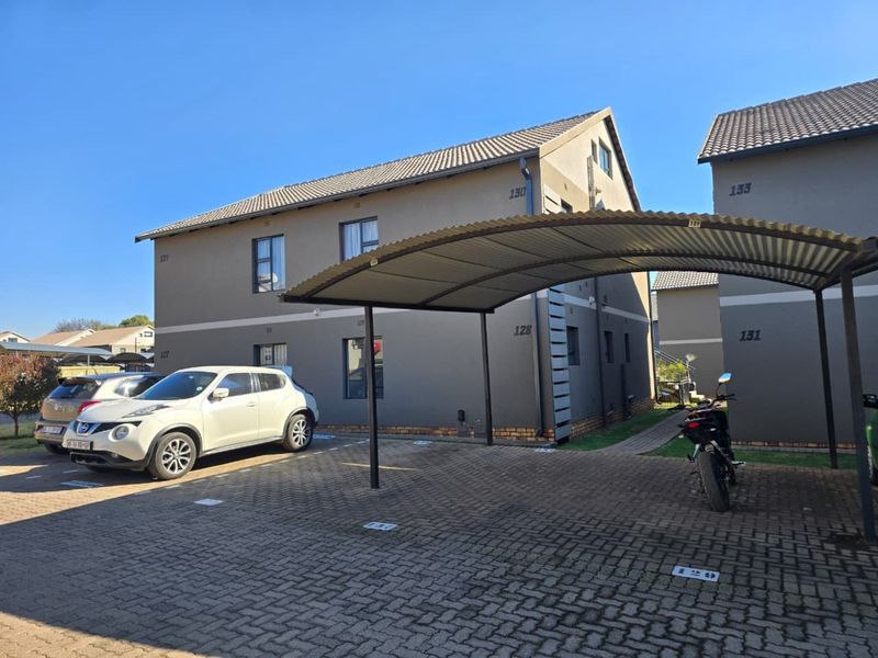 Exterior view of a townhouse complex featuring paved parking areas with covered carports and numbered residential units.