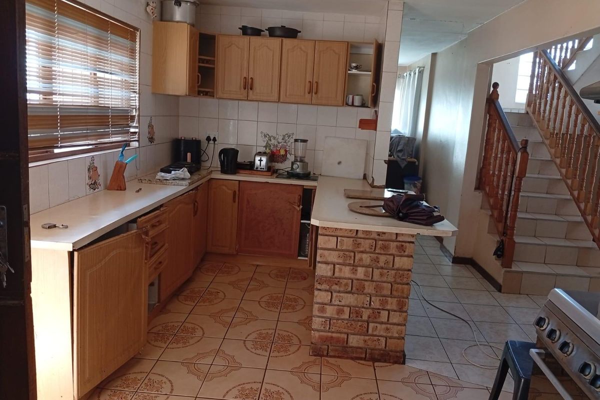 A dated kitchen featuring laminate cabinetry, a brick breakfast bar, and tiled flooring, adjacent to an open staircase.