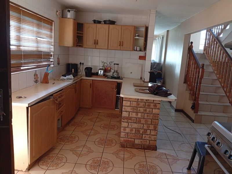 A dated kitchen featuring laminate cabinetry, a brick breakfast bar, and tiled flooring, adjacent to an open staircase.