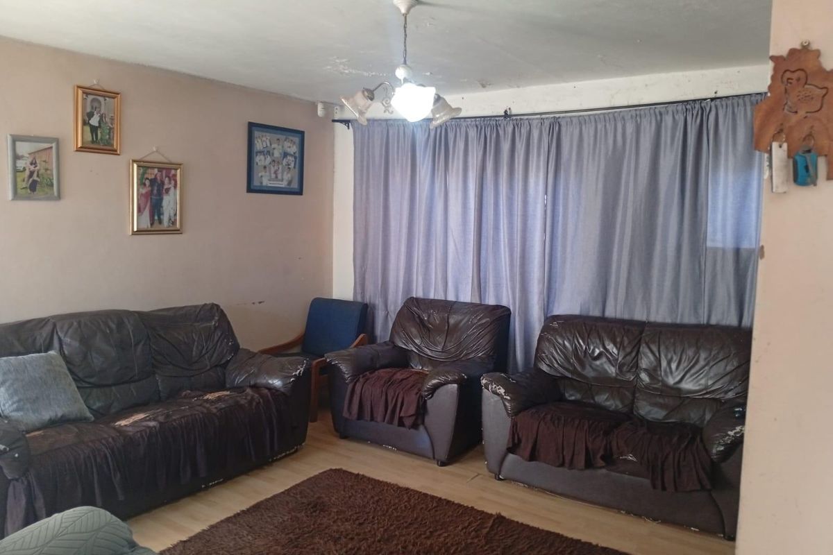 A living room featuring laminate flooring and a central ceiling light fixture, showing signs of wear on the ceiling and walls.