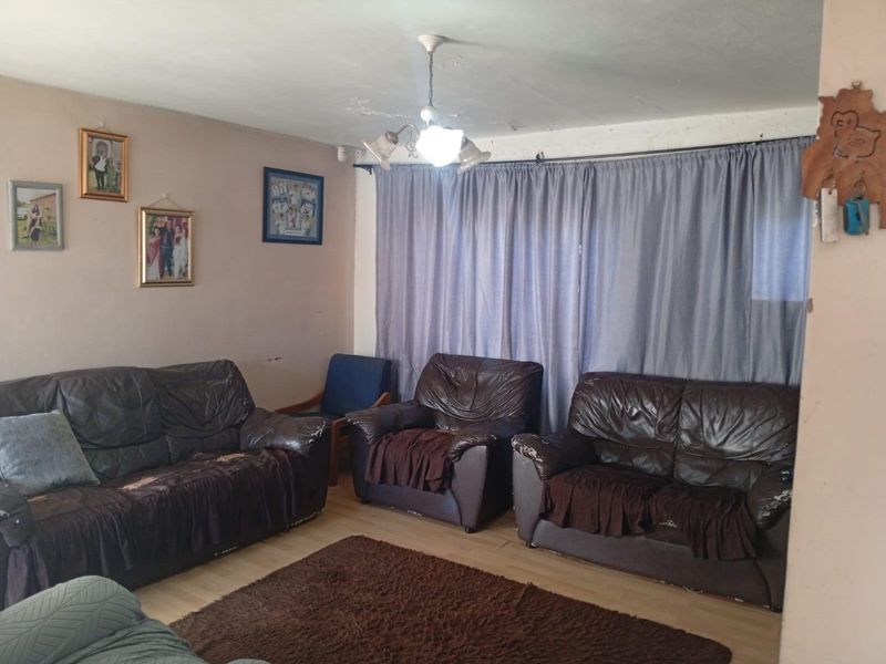 A living room featuring laminate flooring and a central ceiling light fixture, showing signs of wear on the ceiling and walls.