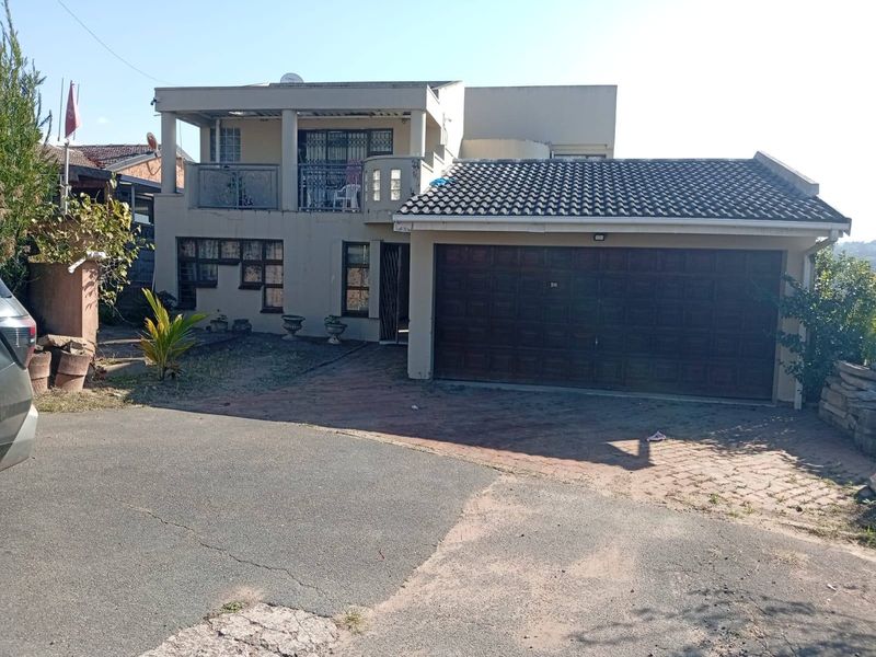 Front elevation of a two-story house featuring a double garage, paved driveway, and an upper-level balcony with security gates.