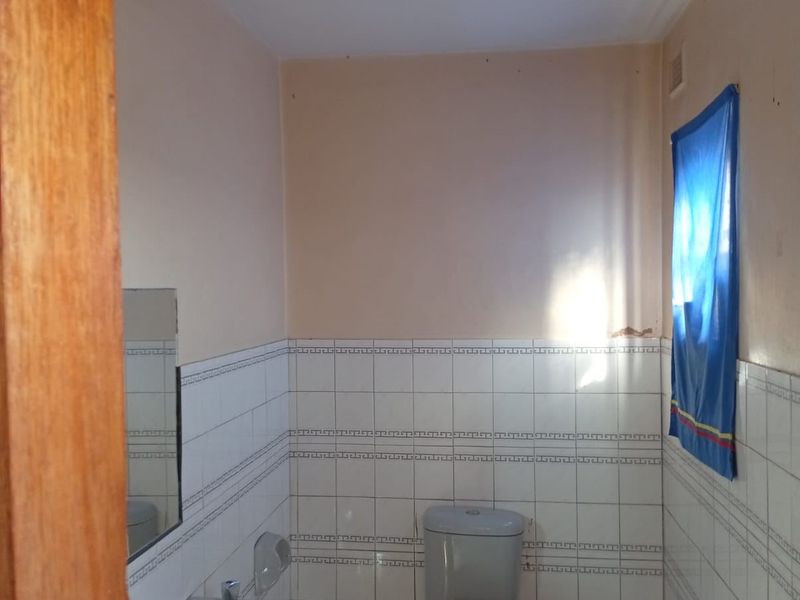 A functional bathroom featuring a pedestal washbasin, toilet, and partial wall tiling. The space requires cosmetic updates and improved lighting fixtures.
