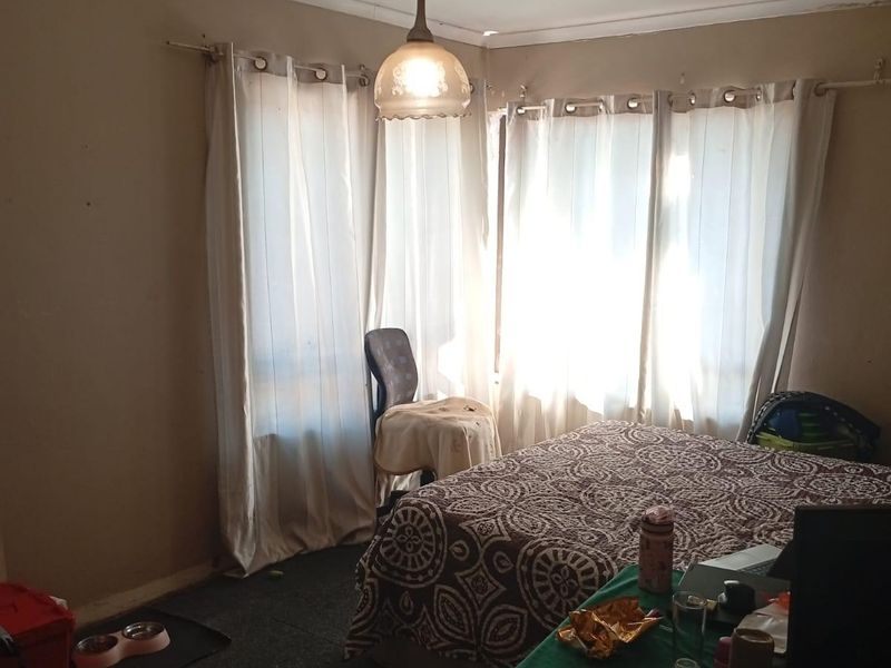 A bedroom featuring a pendant light and large windows with curtain rods, currently showing signs of ceiling damage and wear.