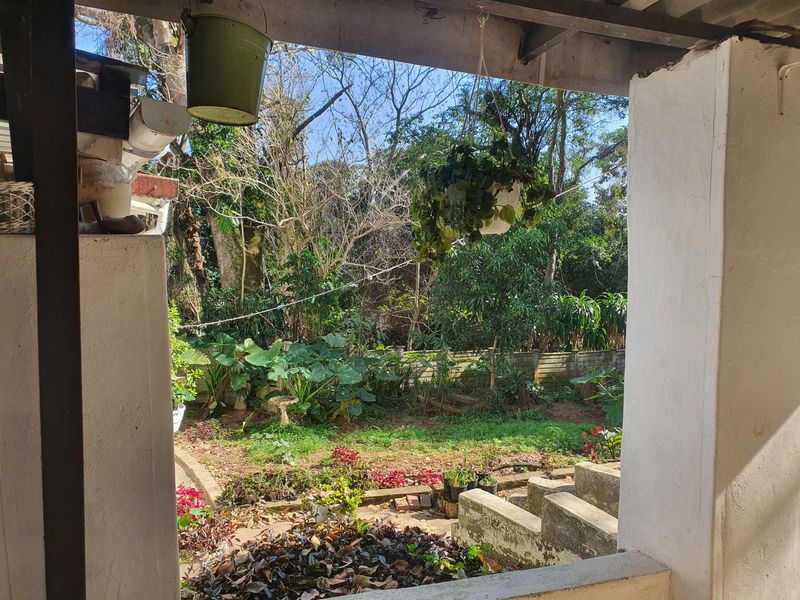 A covered patio area overlooking a garden, featuring concrete steps and masonry pillars in need of maintenance and cosmetic updates.
