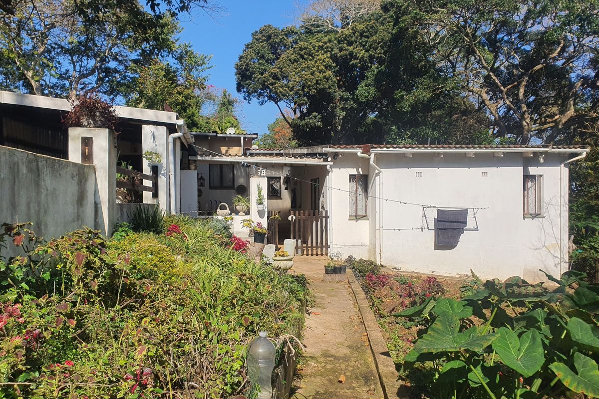 Rear view of the townhouse featuring a concrete pathway, established garden beds, and exterior wall access with mature trees in the background.