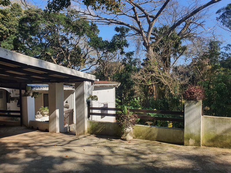 Front exterior view of the townhouse featuring a covered carport, concrete driveway, and a masonry boundary wall with timber fencing.