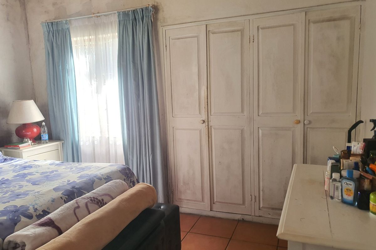 A bedroom featuring built-in cupboards and tiled flooring, currently showing significant wear and tear on the wall finishes.