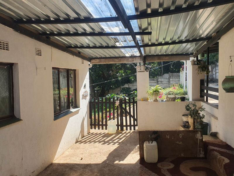 A covered outdoor patio area featuring a corrugated metal roof, concrete flooring, and a timber gate leading to the rear garden.