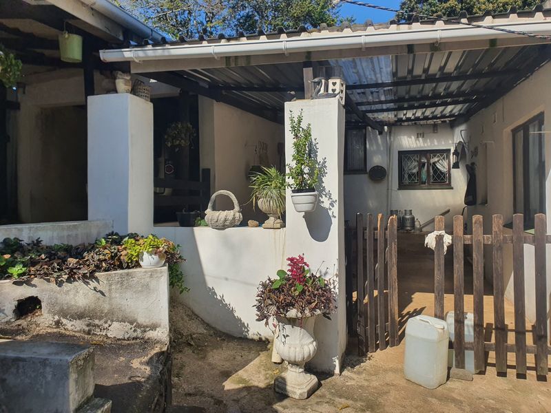 A covered outdoor patio area featuring masonry pillars, a timber gate, and a corrugated roof, offering a rustic entrance space.