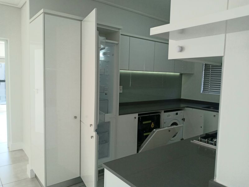 Modern kitchen featuring sleek white cabinetry, integrated appliances, stone countertops, and a glass splashback, offering a clean and functional culinary space.