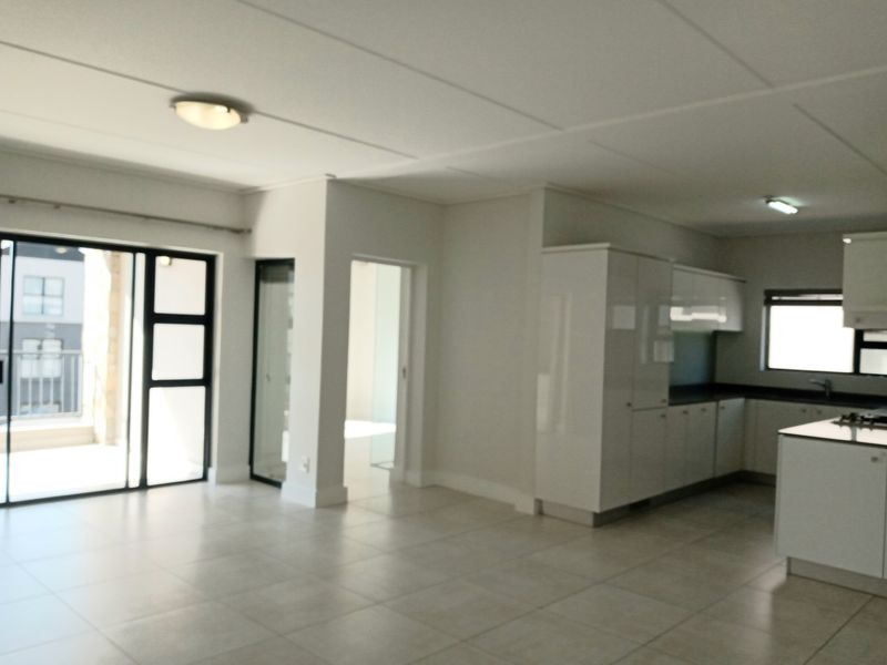 Spacious open-plan living area featuring modern white kitchen cabinetry, stone countertops, tiled flooring, and direct access to a private balcony through sliding glass doors.