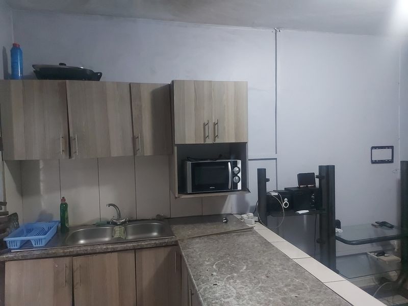 A compact kitchen featuring laminate cabinetry, a double bowl stainless steel sink, and a tiled backsplash with a built-in microwave.