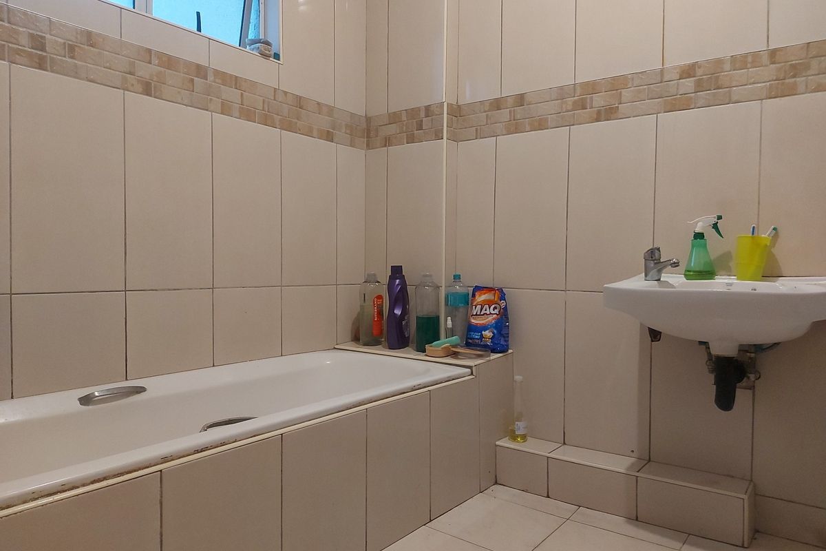 A functional bathroom featuring a built-in bathtub, wall-mounted basin, and neutral ceramic tiling throughout.