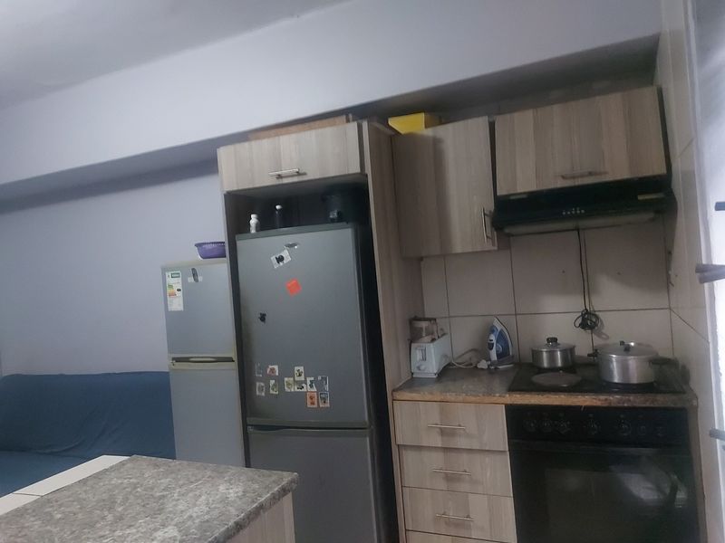 Compact kitchen featuring wood-look cabinetry, built-in oven with hob, extractor fan, and tiled backsplash, providing a functional cooking space.